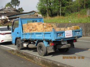 (公社)全日本不動産協会緊急車両の支援物資トラックとその奥の倒壊家屋